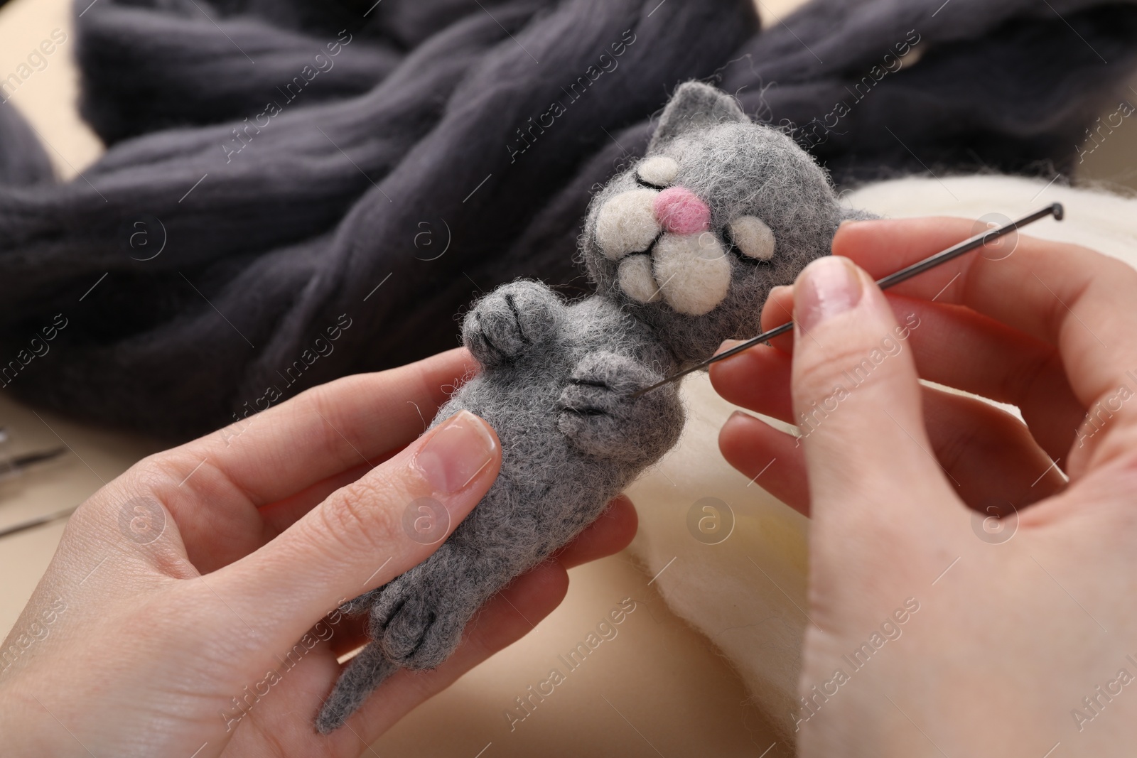 Photo of Woman felting cute toy cat from wool at table, closeup