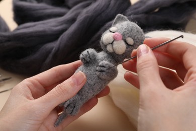 Photo of Woman felting cute toy cat from wool at table, closeup