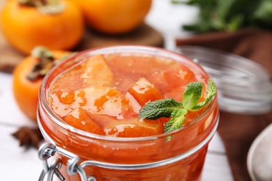 Jar of tasty persimmon jam and mint on table, closeup