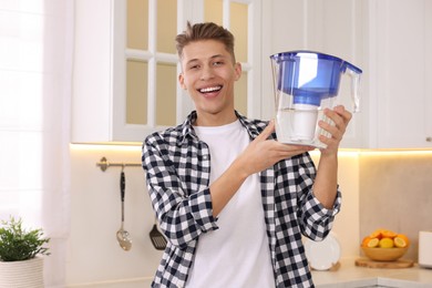 Happy man with water filter jug in kitchen