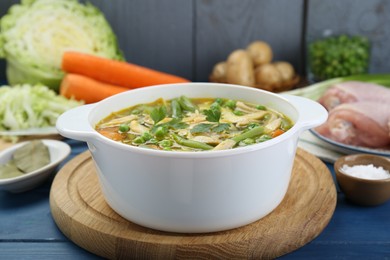 Photo of Saucepan of delicious vegetable soup with chicken and different ingredients on blue wooden table