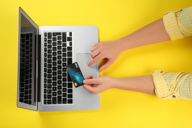 Online payment. Woman using credit card and laptop at yellow table, top view