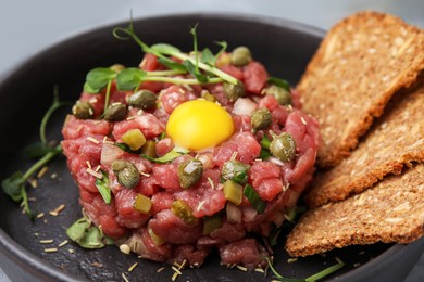 Photo of Tasty beef steak tartare served with yolk, capers and bread in serving pan, closeup