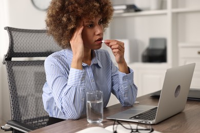 Photo of Woman taking pill while suffering from headache at workplace in office