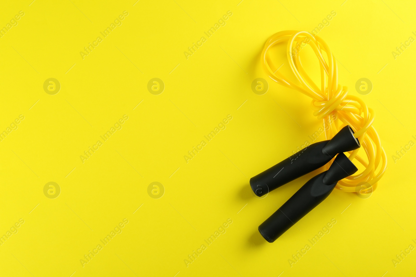 Photo of Skipping rope on yellow background, top view. Space for text