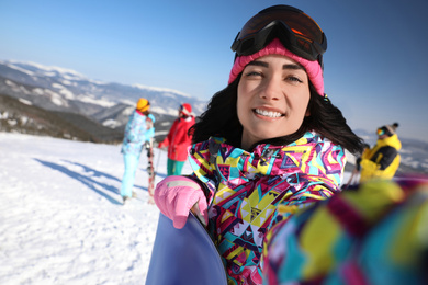 Photo of Young woman with snowboard taking selfie at ski resort. Winter vacation