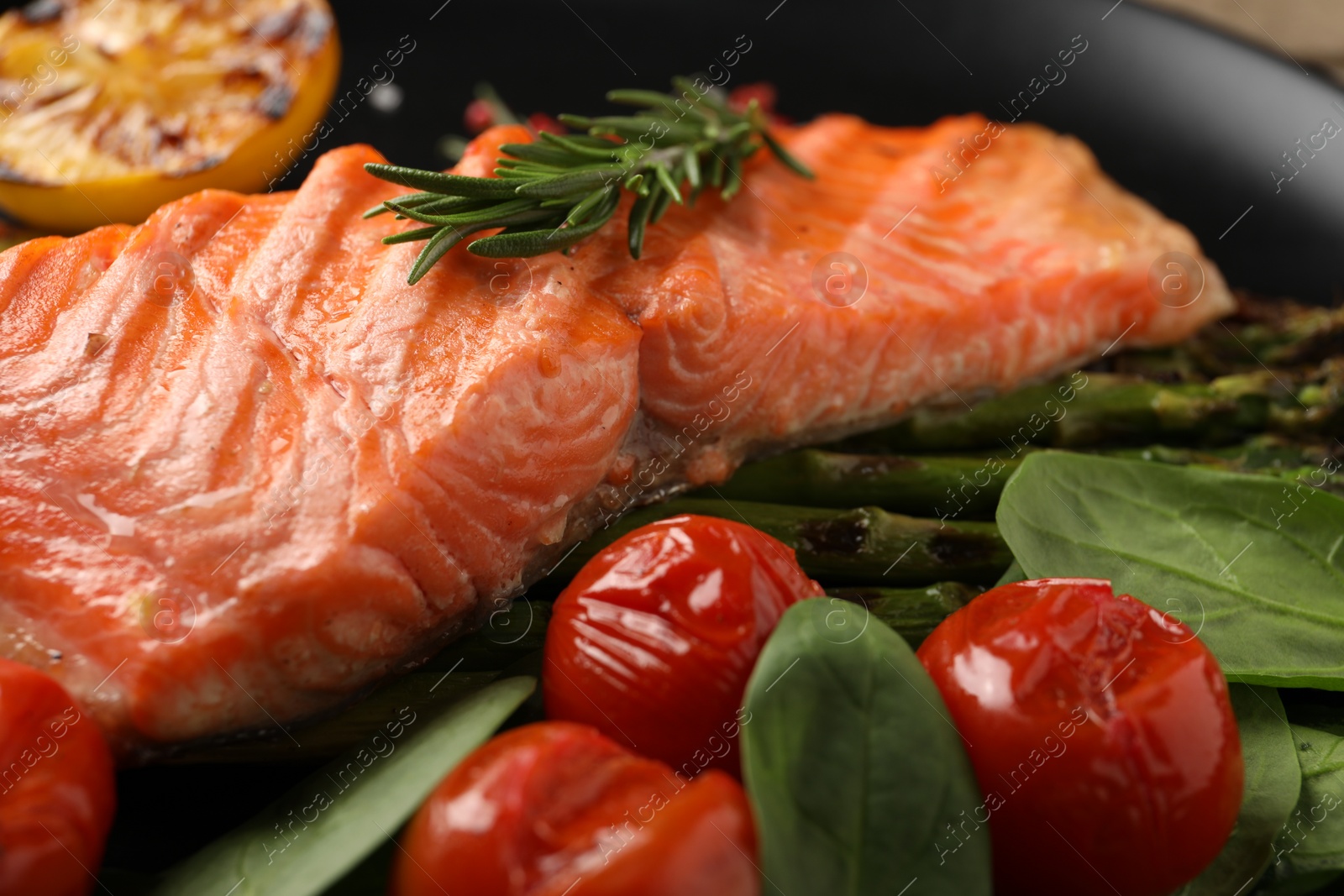 Photo of Tasty grilled salmon with tomatoes, spinach and rosemary on plate, closeup