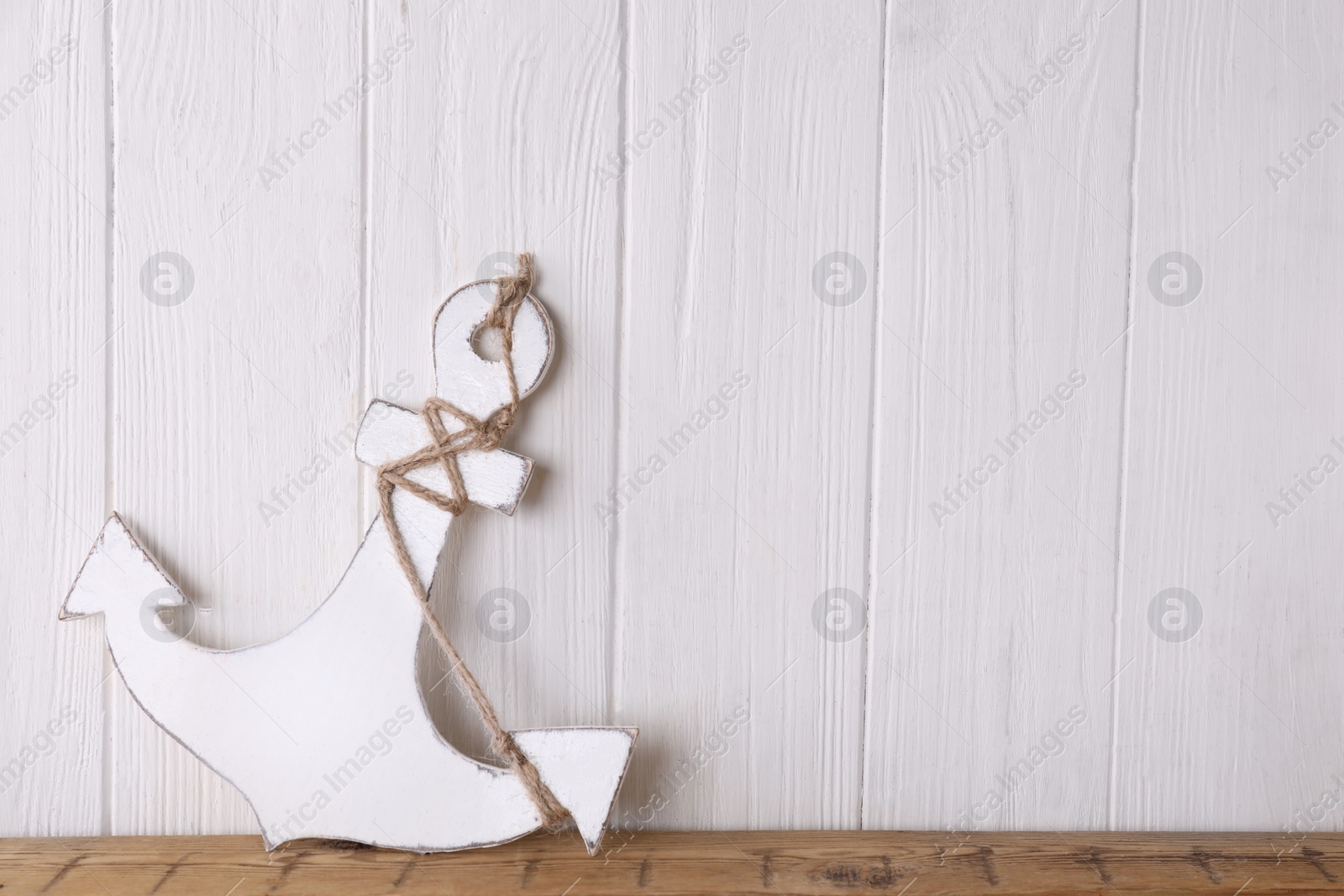 Photo of Anchor with hemp rope on table near white wooden wall, space for text