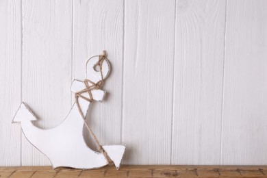 Photo of Anchor with hemp rope on table near white wooden wall, space for text