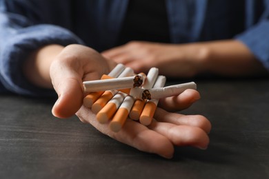 Stop smoking. Woman holding whole and broken cigarettes at black table, closeup