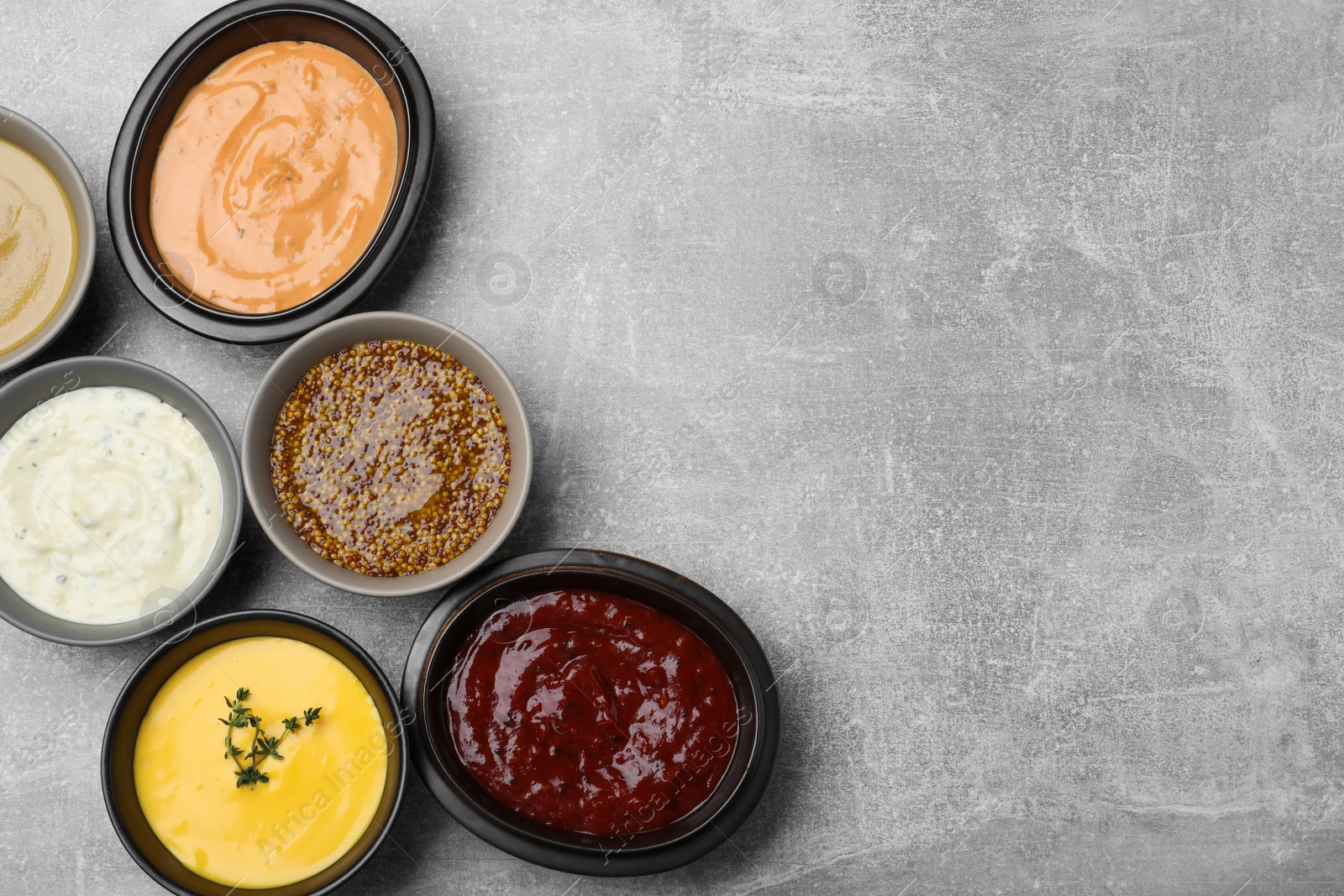 Photo of Many different sauces on grey table, flat lay. Space for text