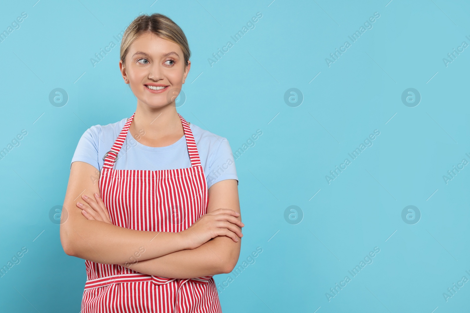 Photo of Beautiful young woman in clean striped apron on light blue background. Space for text