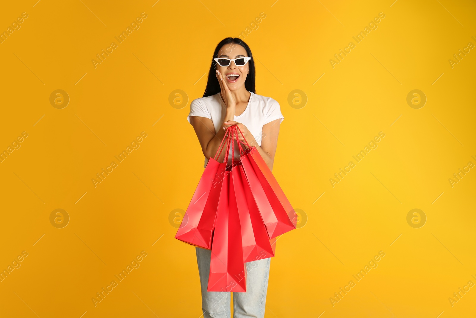 Photo of Beautiful young woman with paper shopping bags on yellow background