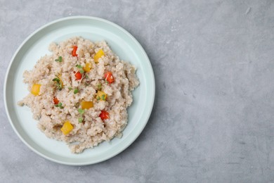 Photo of Delicious barley porridge with vegetables and microgreens on gray table, top view. Space for text