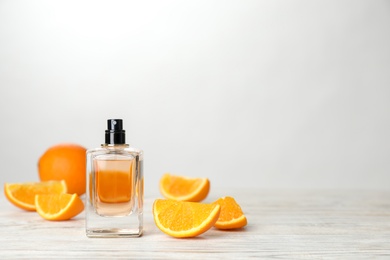 Photo of Bottle of perfume and orange on table against light background