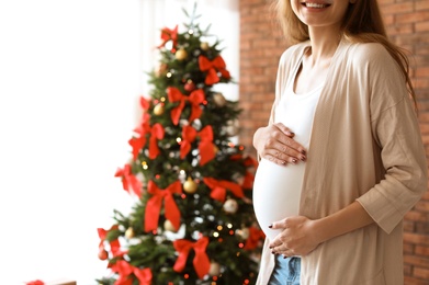 Photo of Pregnant woman near Christmas tree at home. Expecting baby
