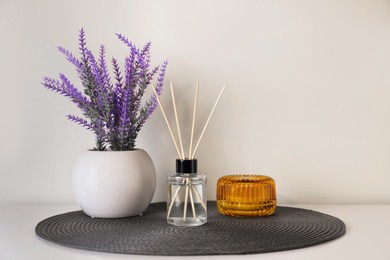 Photo of Aromatic reed air freshener, candle and lavender flowers on white table