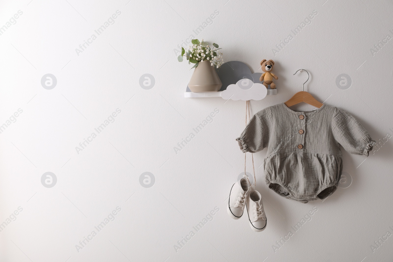 Photo of Cute baby onesie and shoes hanging on white wall. Space for text