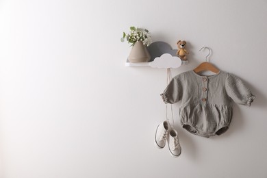 Photo of Cute baby onesie and shoes hanging on white wall. Space for text