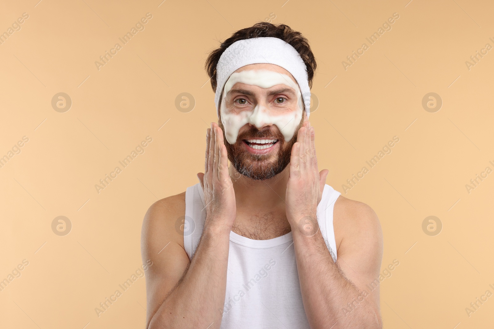 Photo of Man with headband washing his face on beige background