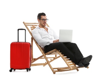 Young businessman with laptop and suitcase on sun lounger against white background. Beach accessories