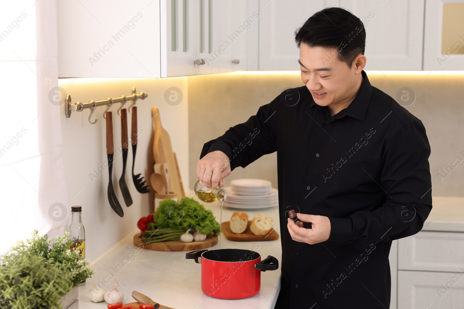 Photo of Cooking process. Man pouring oil into pot at countertop in kitchen