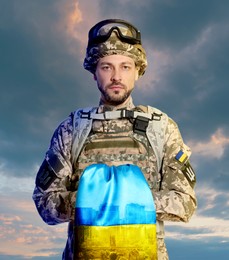 Soldier in military uniform with Ukrainian flag against cloudy sky