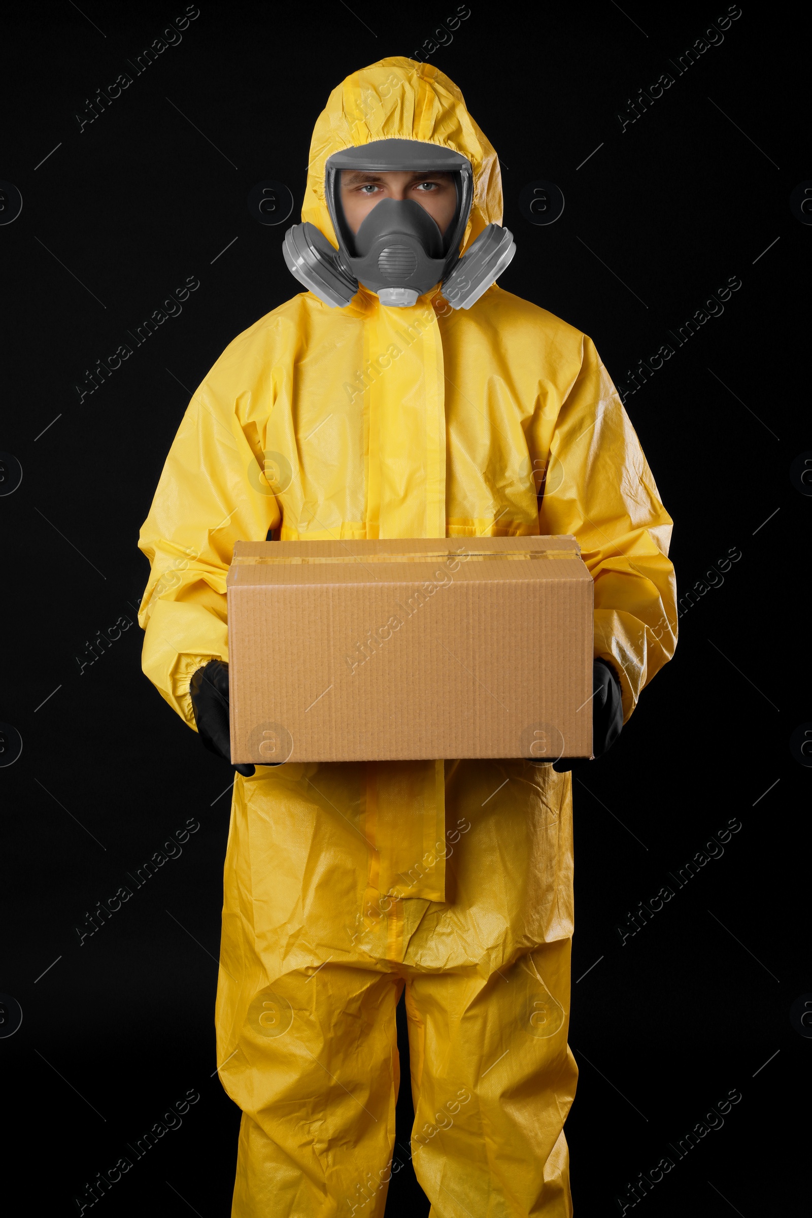 Photo of Man wearing chemical protective suit with cardboard box on black background. Prevention of virus spread