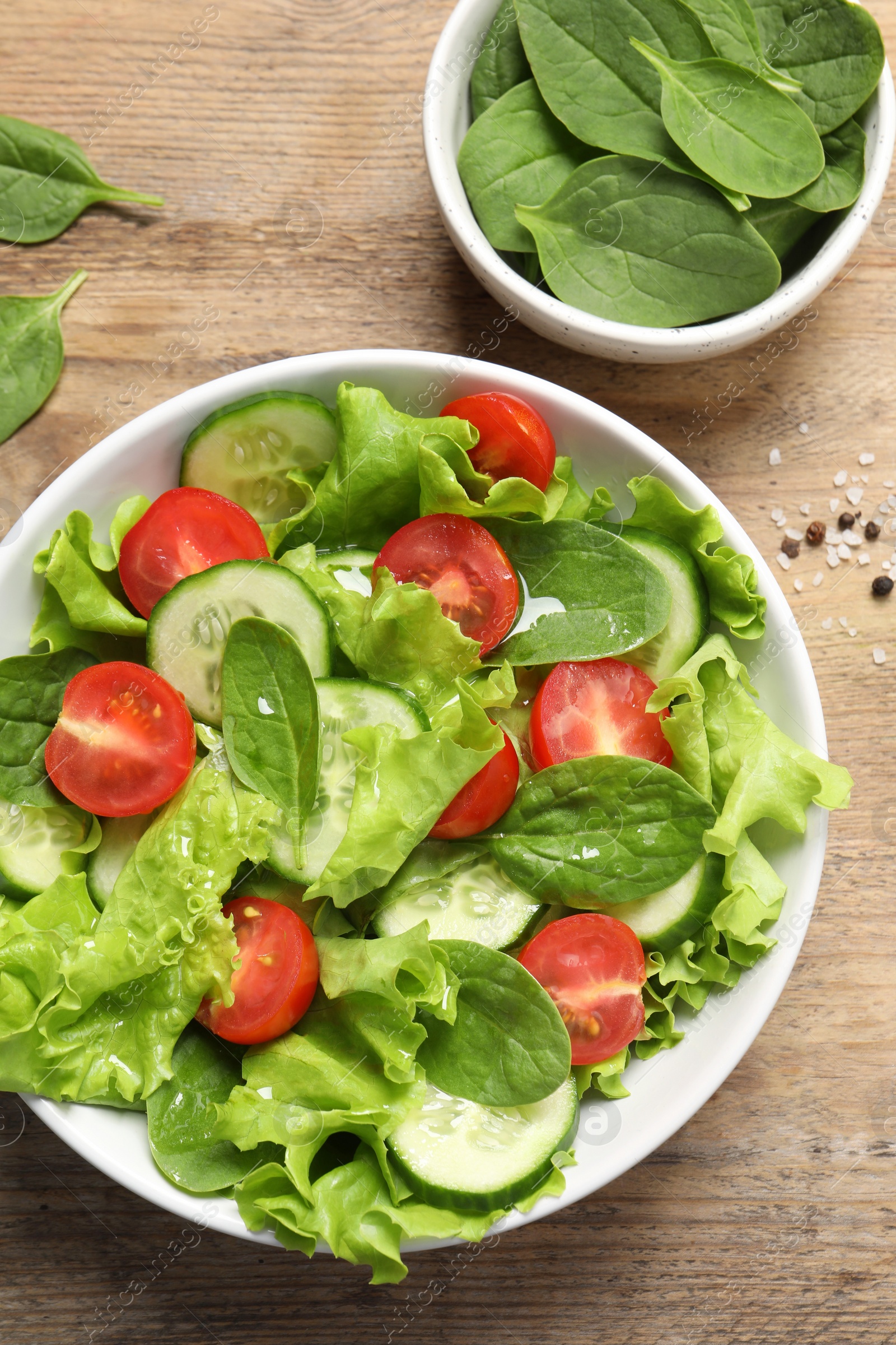 Photo of Delicious vegetable salad and bowl of spinach on wooden table, flat lay