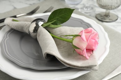 Stylish setting with rose, napkin and plates on table, closeup