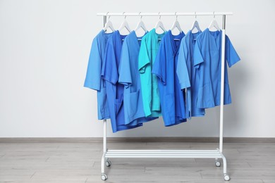 Photo of Different medical uniforms on rack near light grey wall indoors. Space for text