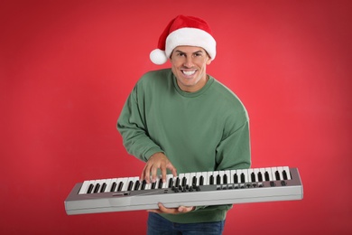 Photo of Man in Santa hat playing synthesizer on red background. Christmas music