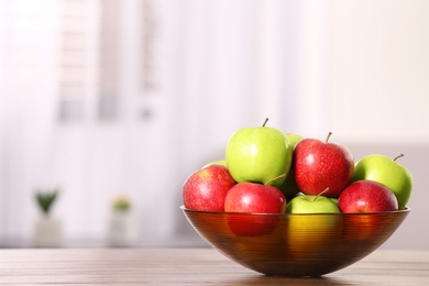 Photo of Bowl with different sweet apples on table in room, space for text