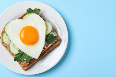 Plate of tasty sandwich with heart shaped fried egg on light blue background, top view. Space for text