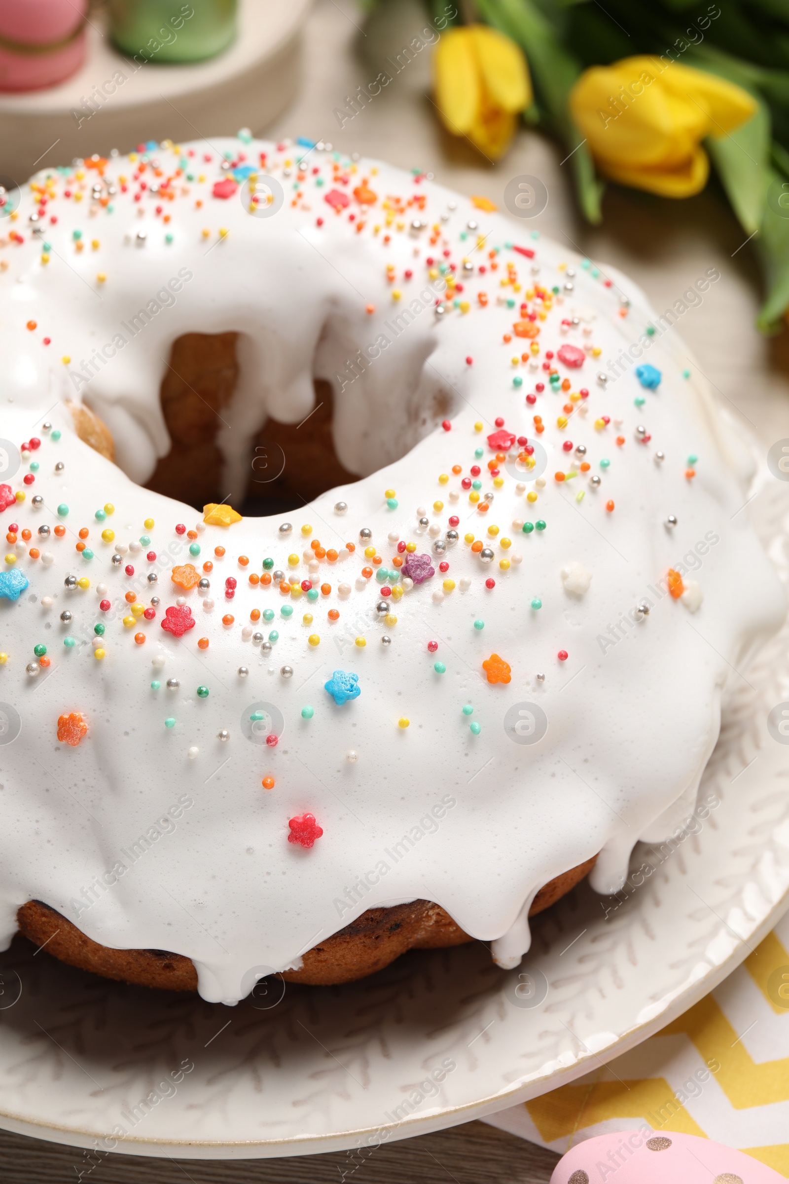 Photo of Easter cake with sprinkles, painted eggs and tulips on wooden table, closeup