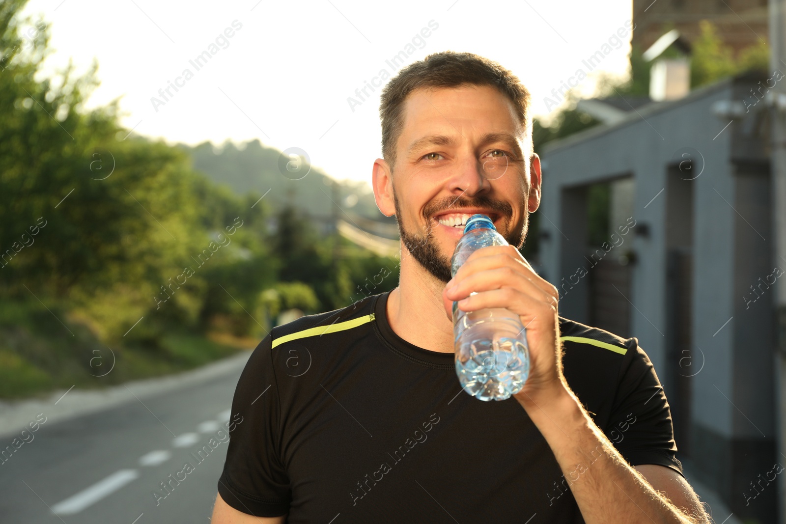 Photo of Happy man drinking water outdoors on hot summer day. Refreshing drink