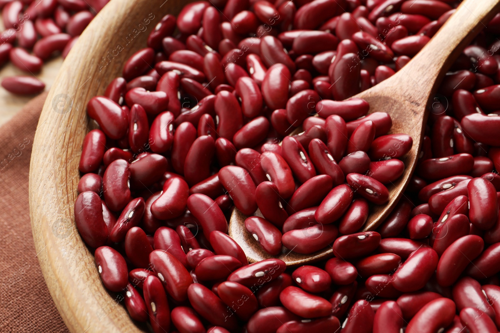 Photo of Raw red kidney beans with spoon in wooden bowl, closeup