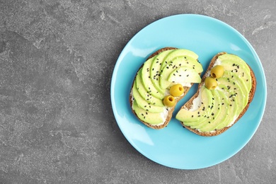 Crisp rye toasts with avocado, cream cheese and olives on plate, top view