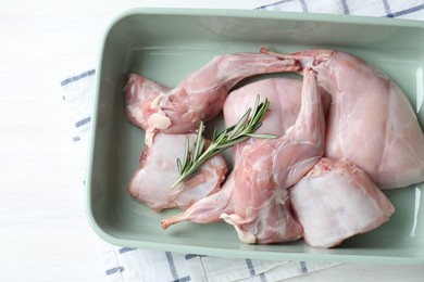 Photo of Raw rabbit meat and rosemary in baking dish on white wooden table, top view