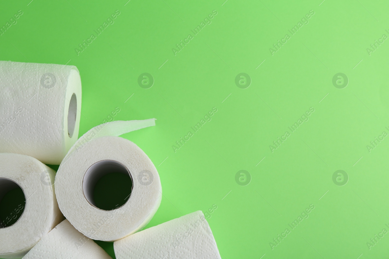 Photo of Soft toilet paper rolls on green background, flat lay. Space for text