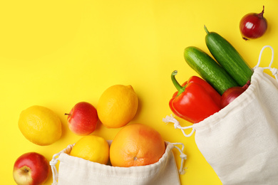 Photo of Cotton eco bags with fruits and vegetables on yellow background, flat lay. Space for text