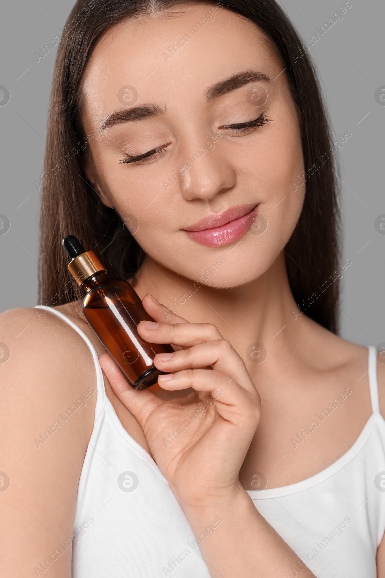 Photo of Beautiful young woman with essential oil on light grey background, closeup