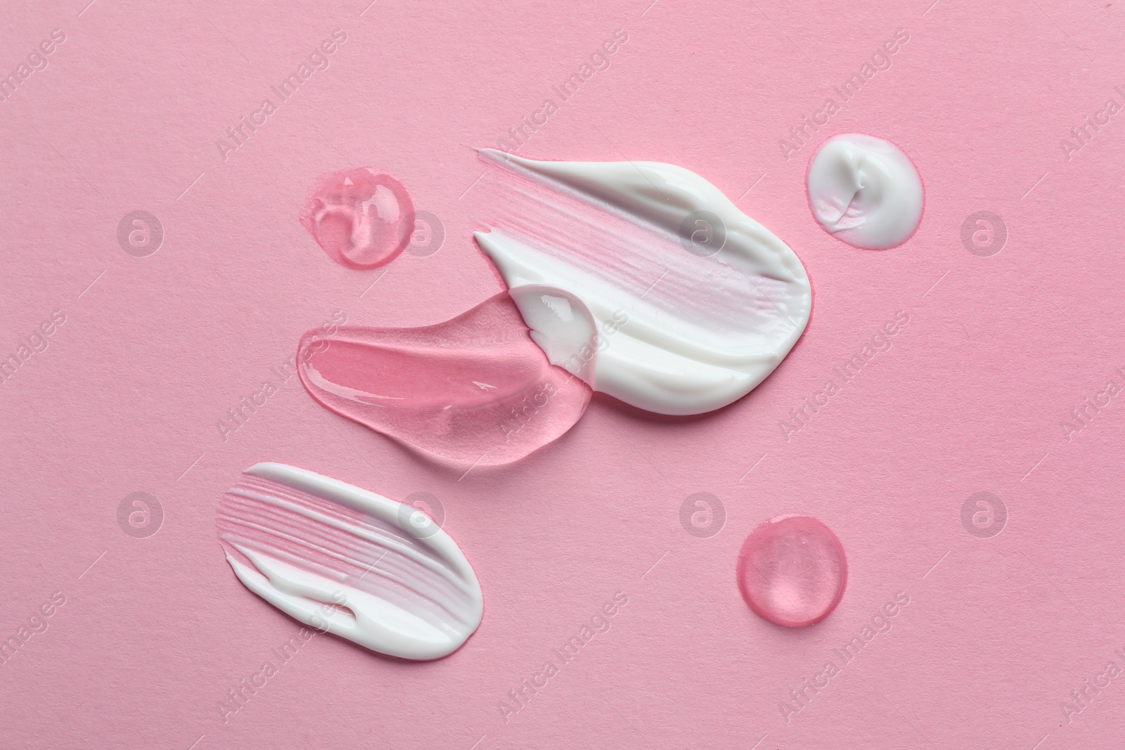 Photo of Samples of transparent gel and white cream on pink background, flat lay