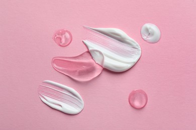 Photo of Samples of transparent gel and white cream on pink background, flat lay