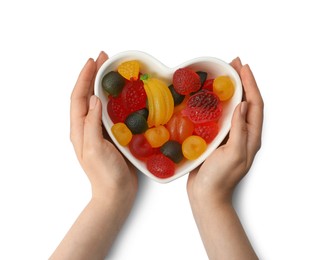 Photo of Woman holding heart shaped bowl with delicious gummy candies on white background, top view