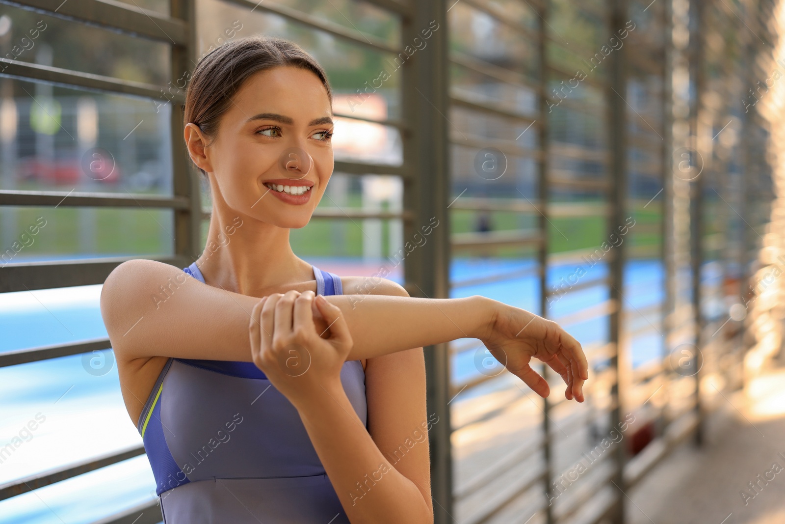 Photo of Attractive happy woman doing exercises on sports ground, space for text. Stretching outdoors