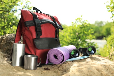 Photo of Modern backpack and camping equipment on large rock in wilderness