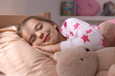 Photo of Cute little girl with toy bear sleeping in bed at home