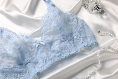 Photo of Light blue women's underwear, perfume and necklace on white fabric, closeup