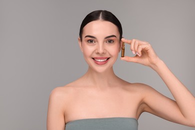 Beautiful young woman holding skincare ampoule on grey background